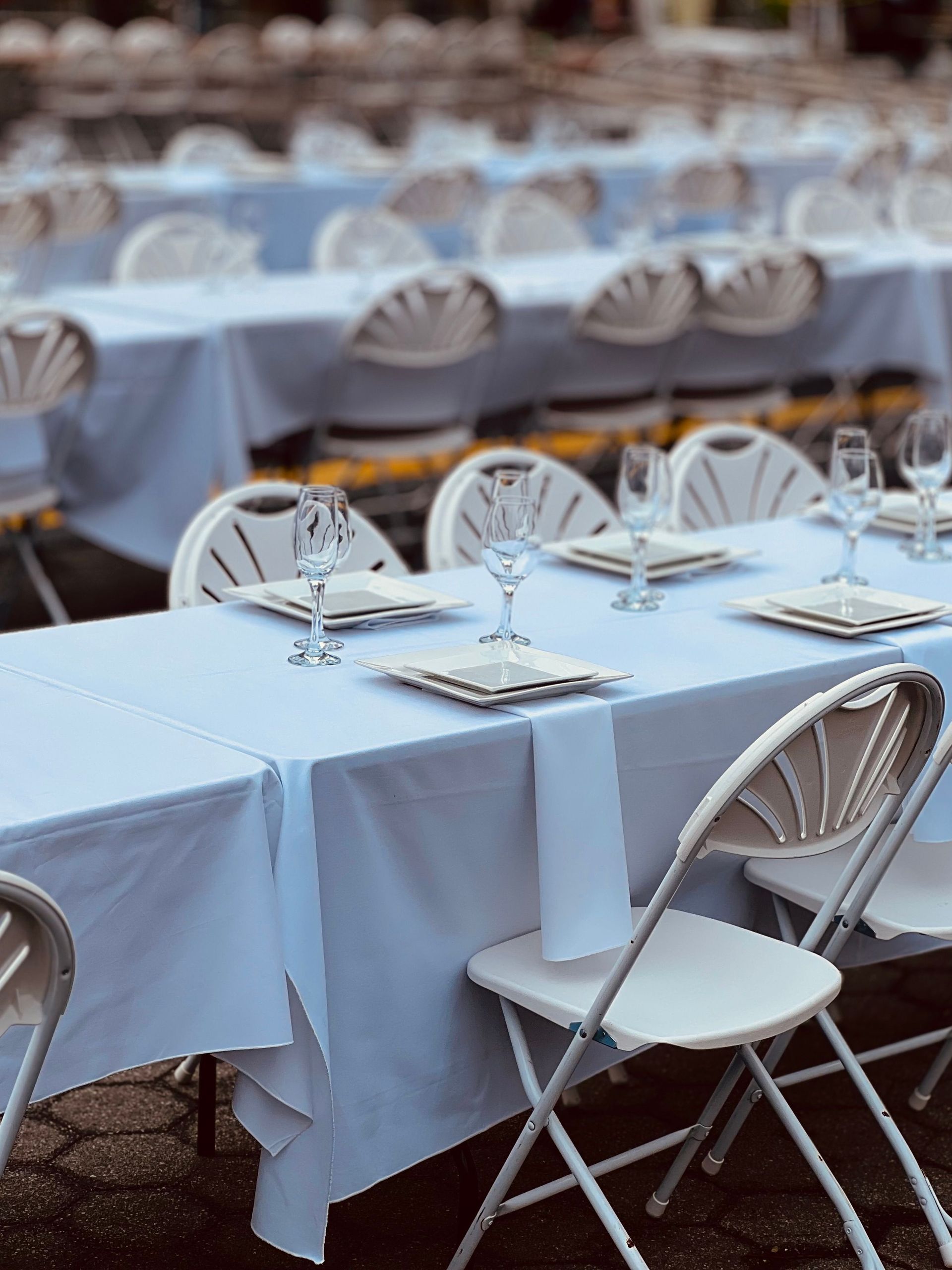 Rows of white tables set for an outdoor event with elegant arrangements.