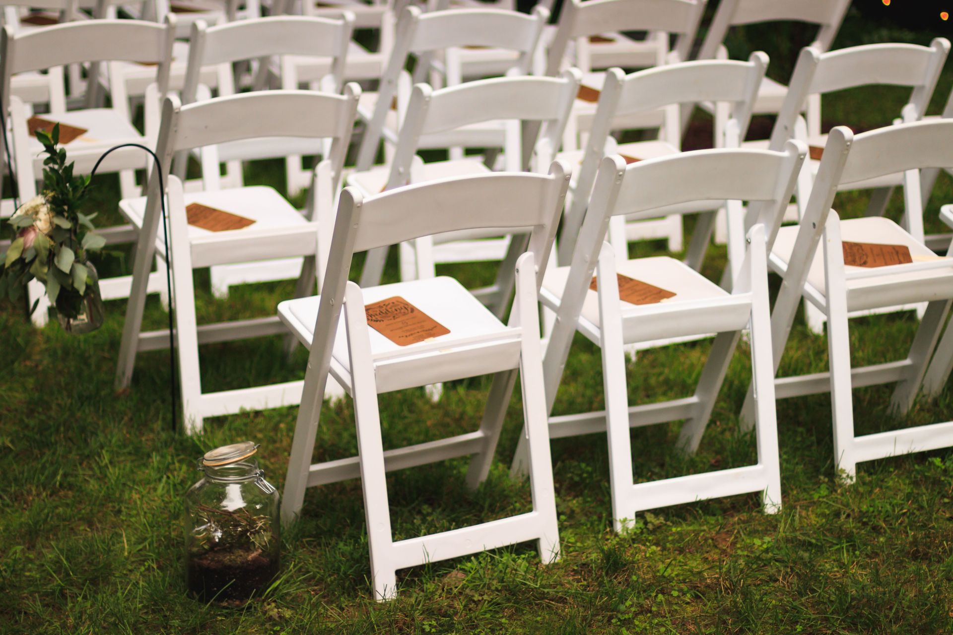 White wooden chairs arranged in a garden setting, perfect for an outdoor wedding or event.