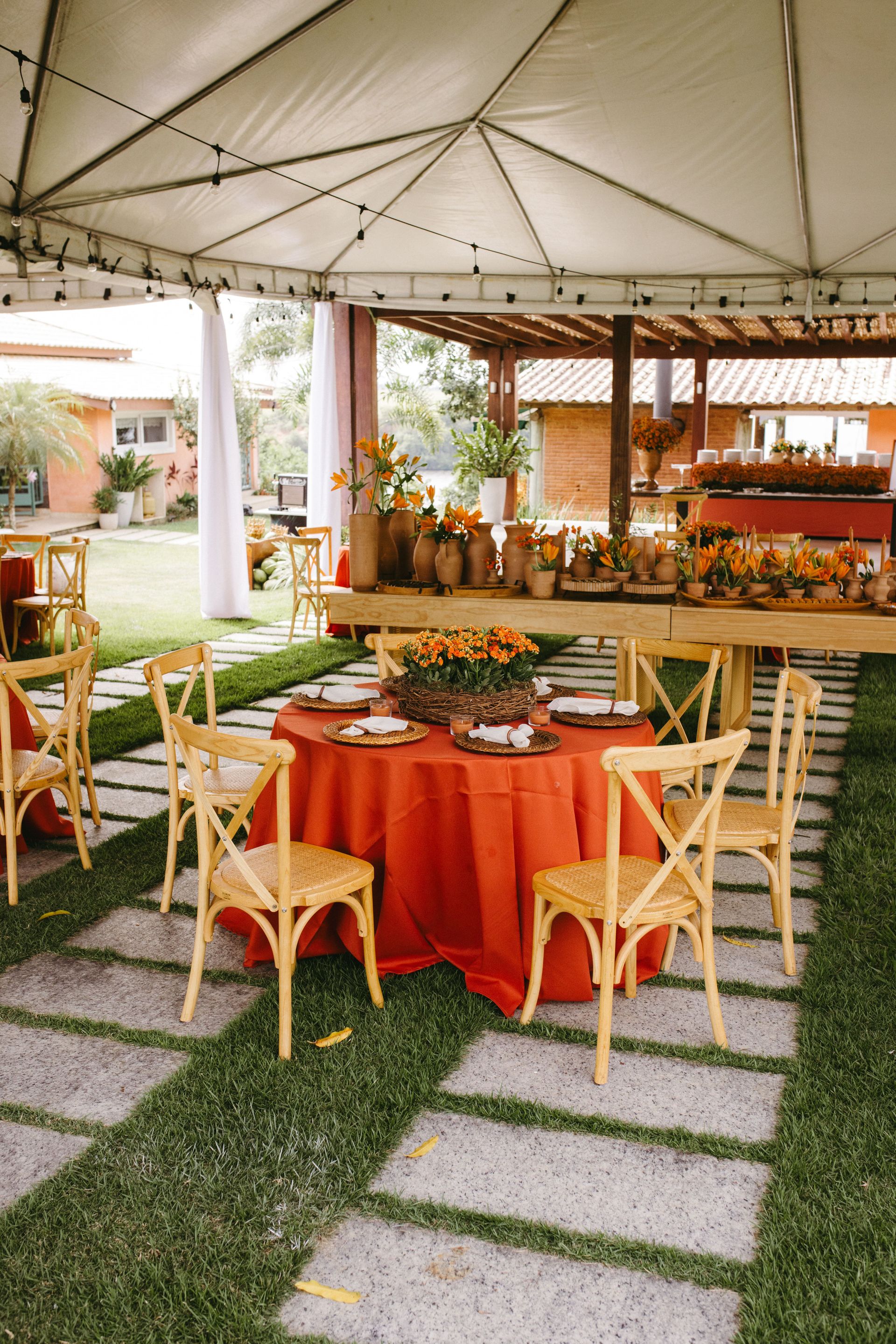 Chic outdoor wedding reception featuring terracotta decor and vibrant orange accents under a tent.