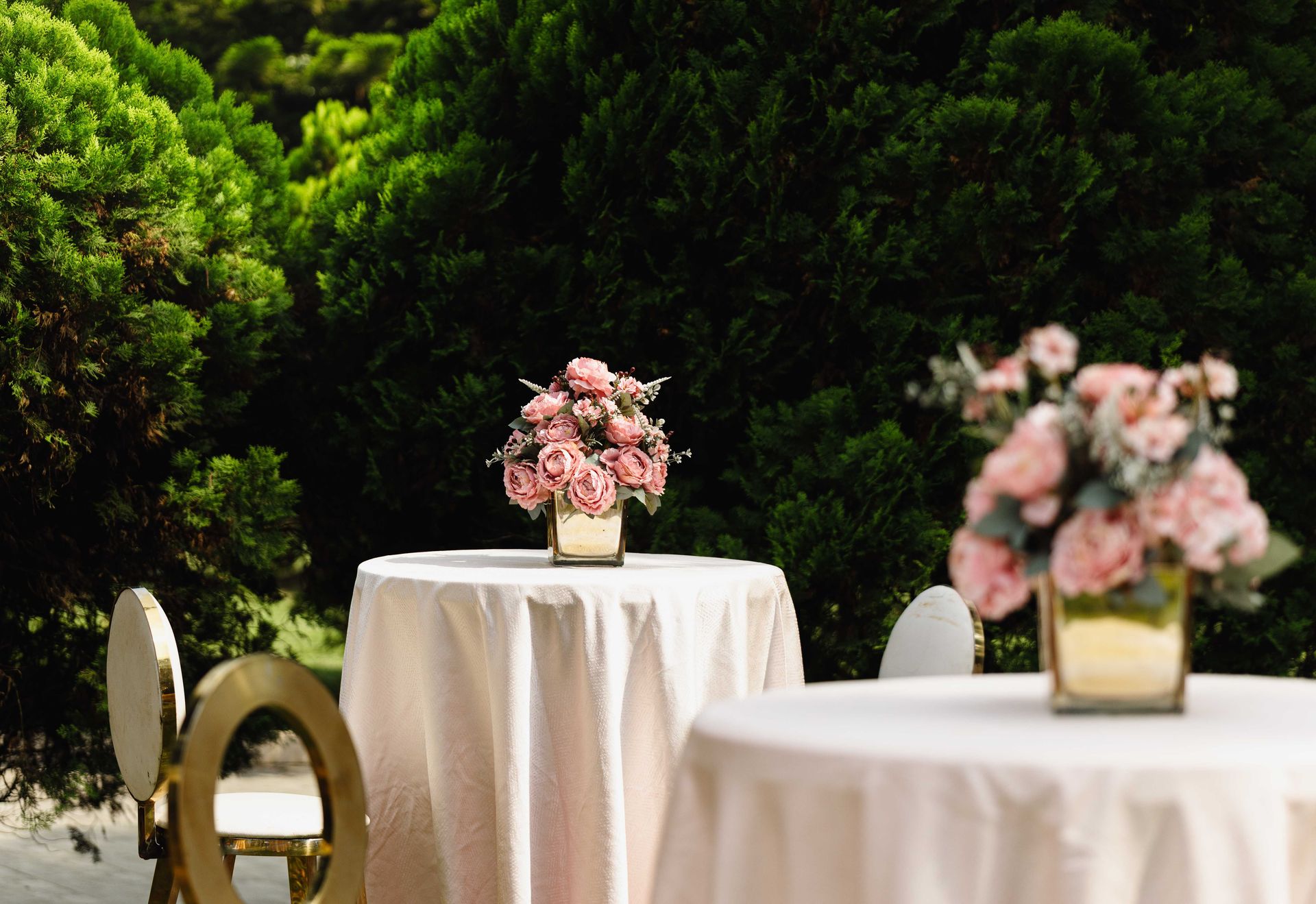 Beautiful outdoor wedding tables set with pink floral arrangements in a lush green garden.