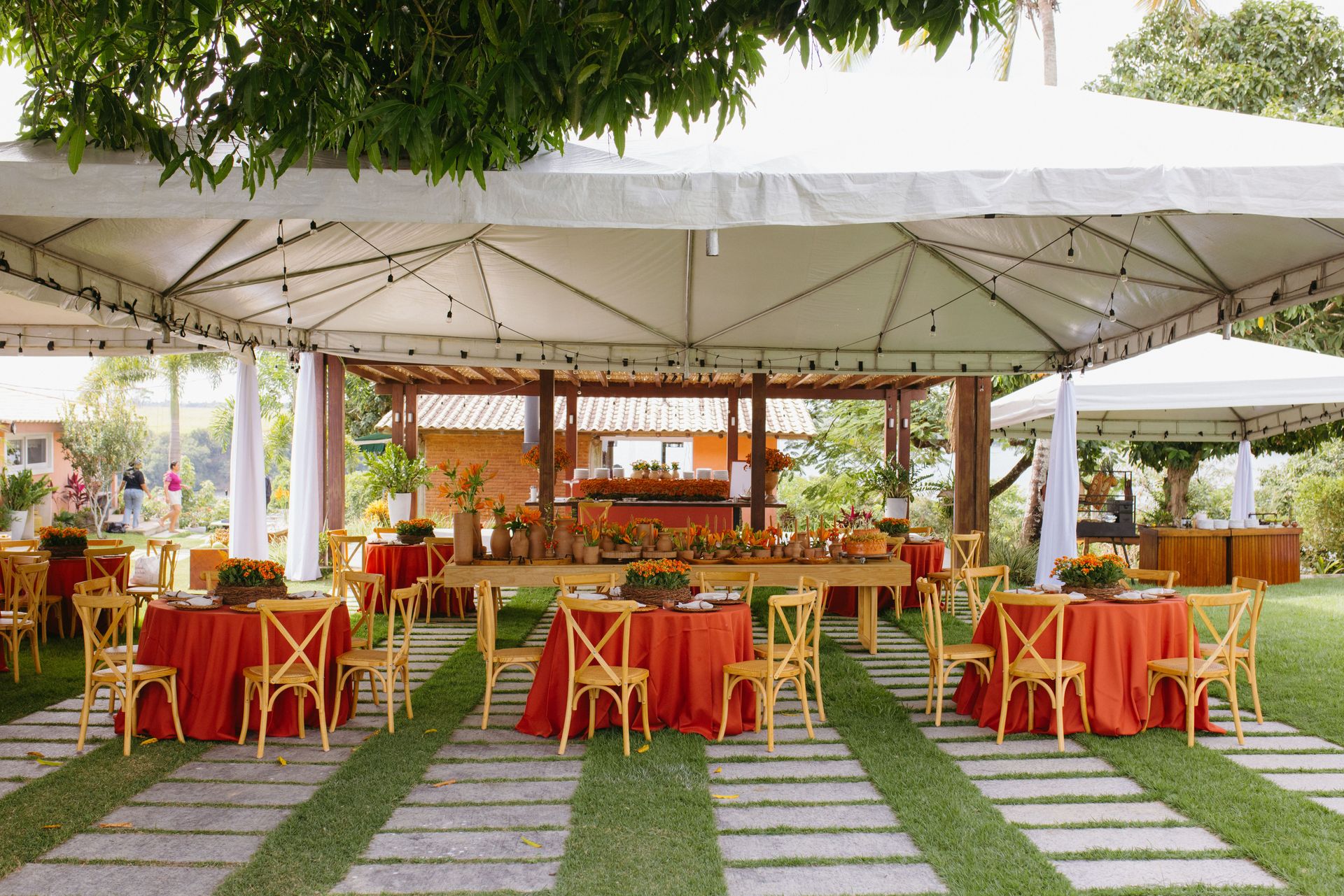 Beautifully arranged outdoor wedding setup with red and orange decor under a white canopy.