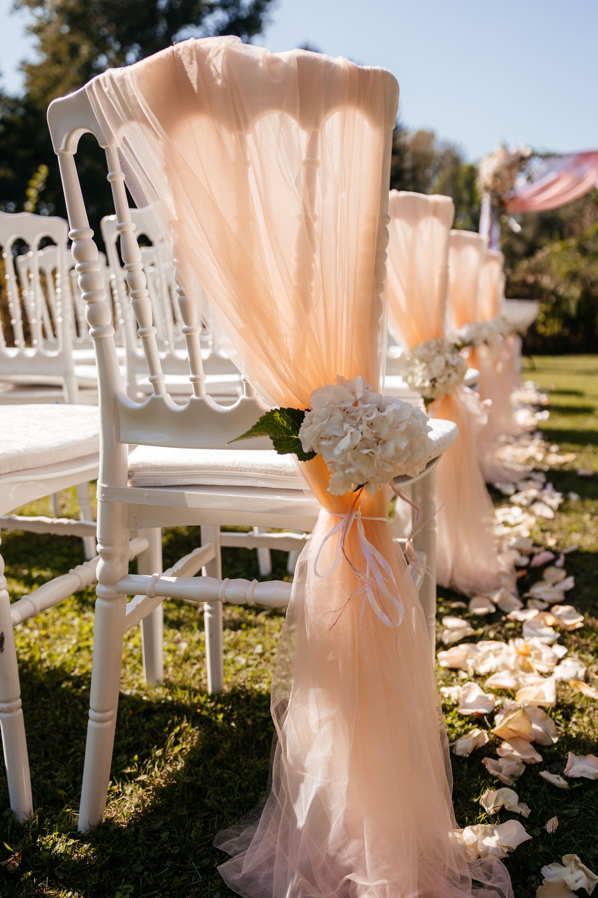Chic outdoor wedding setup with white chairs draped in peach fabric, perfect for a romantic ceremony.