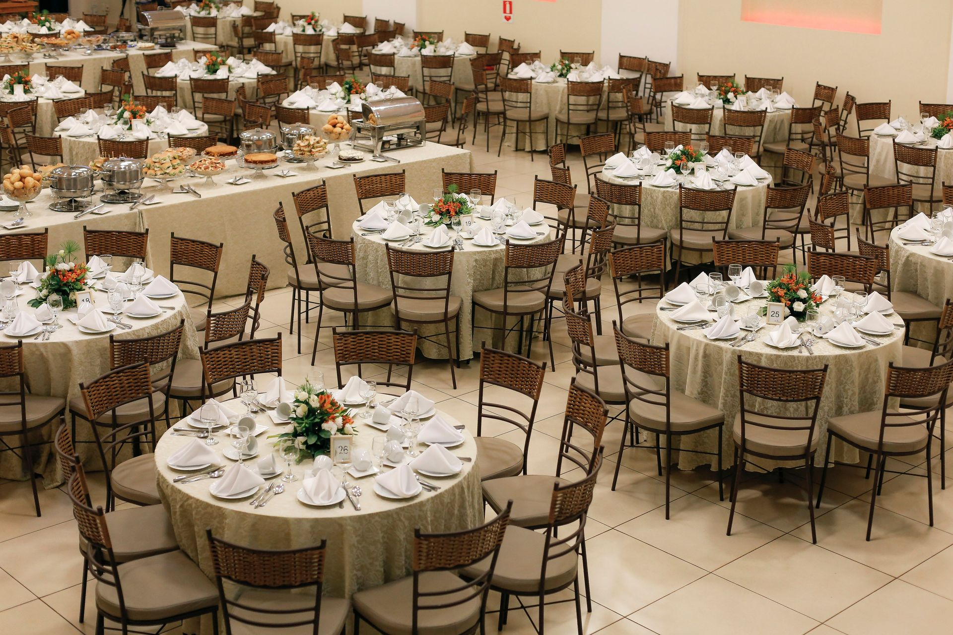 Spacious banquet hall setup with neatly arranged round tables and floral centerpieces, ready for a large event.