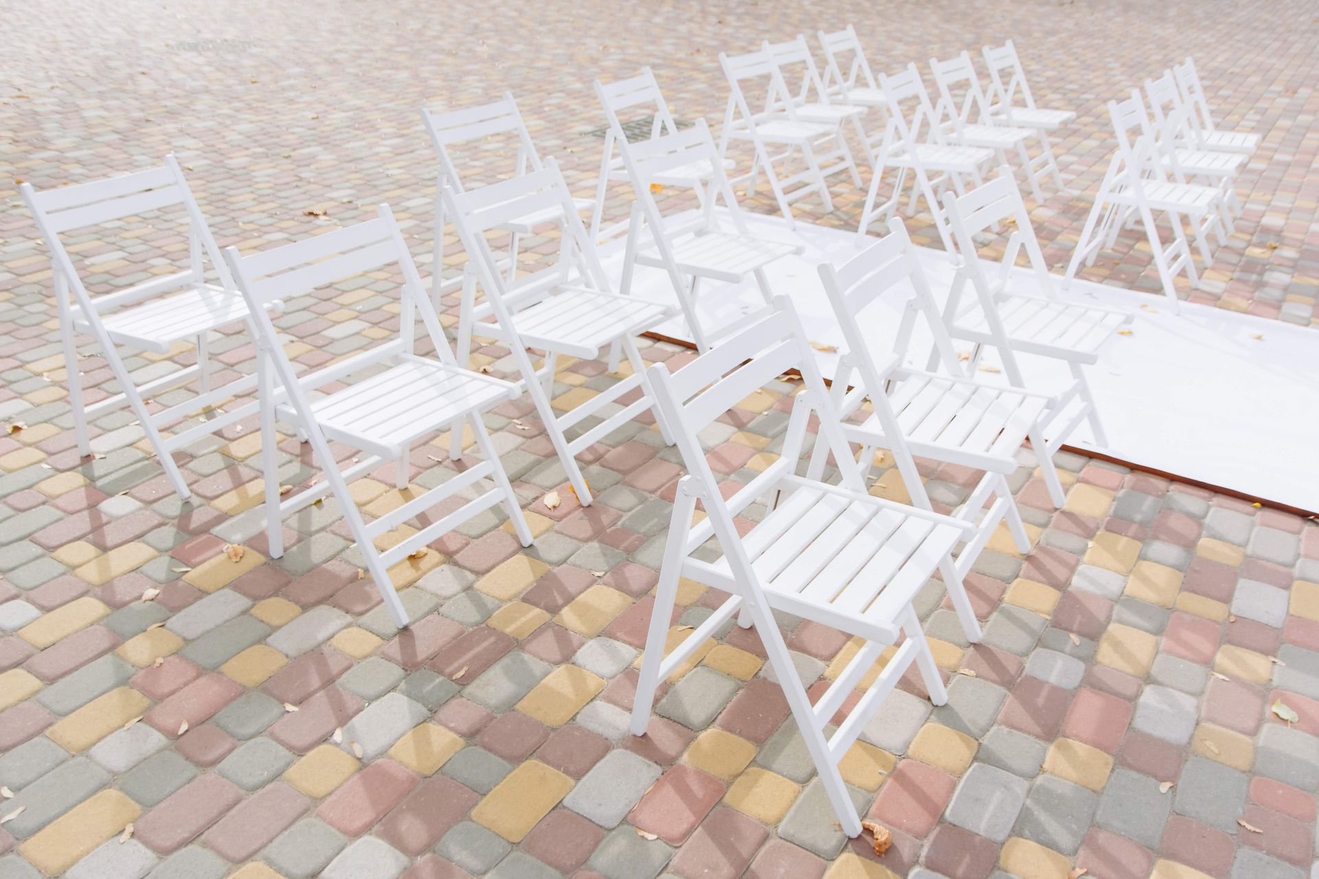 An arrangement of white folding chairs placed on colorful patterned pavers in an outdoor setting.